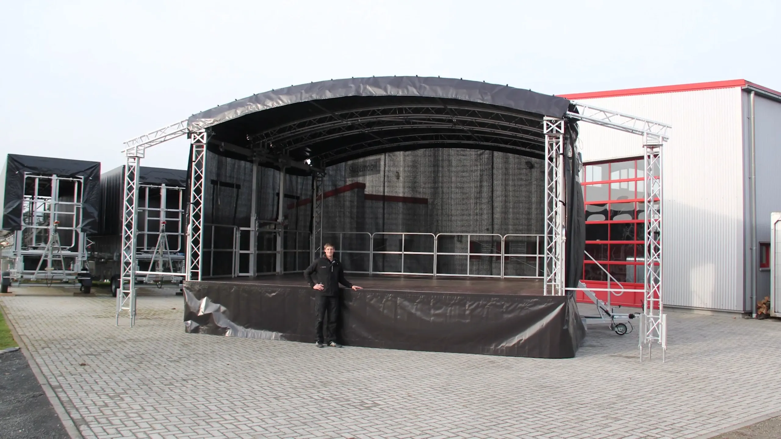Trailer mounted mobile stage with a curved black roof and truss towers on both sides