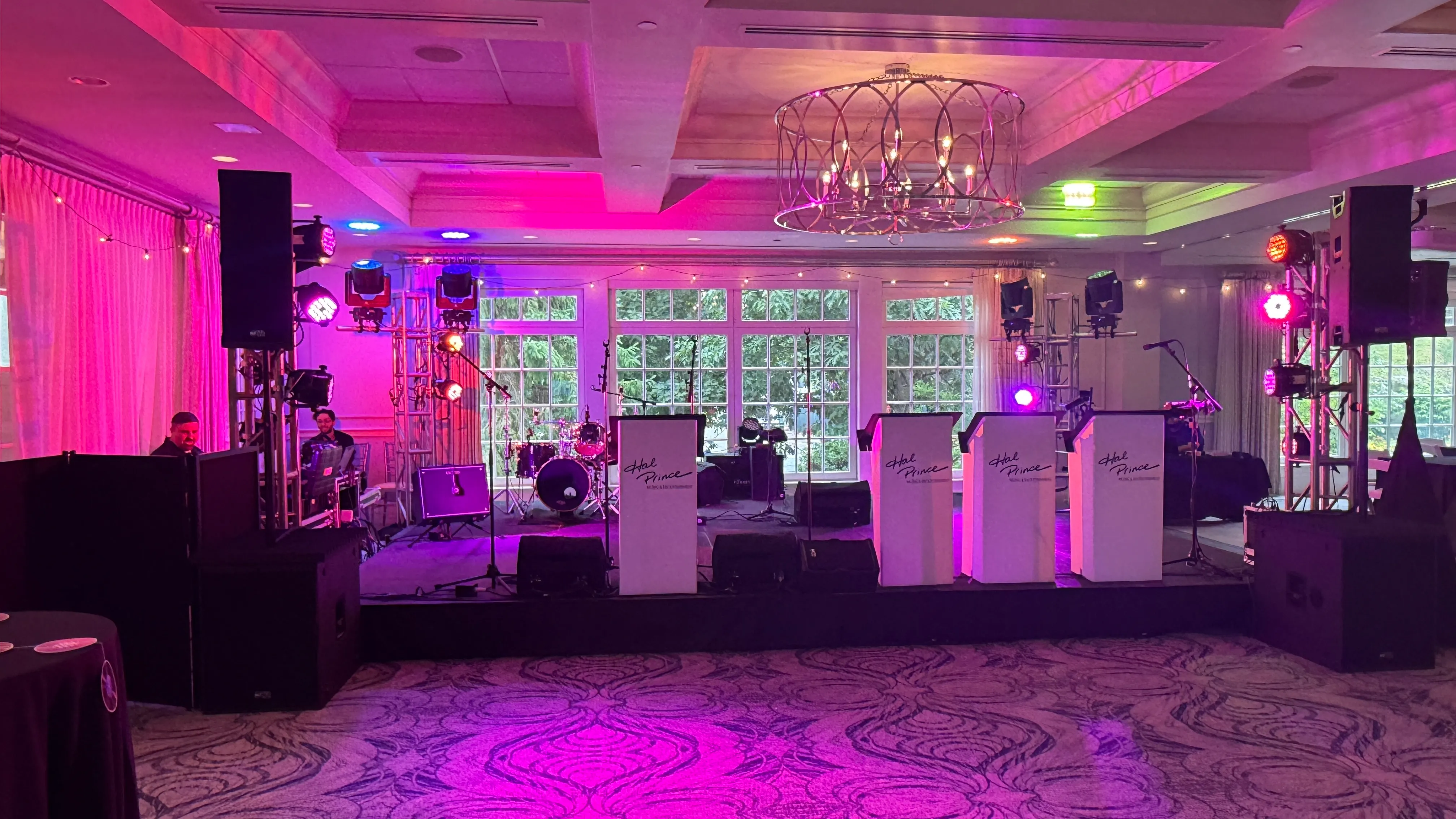 Country club stage set for a live band with a drum kit, PA speakers and pink uplighting