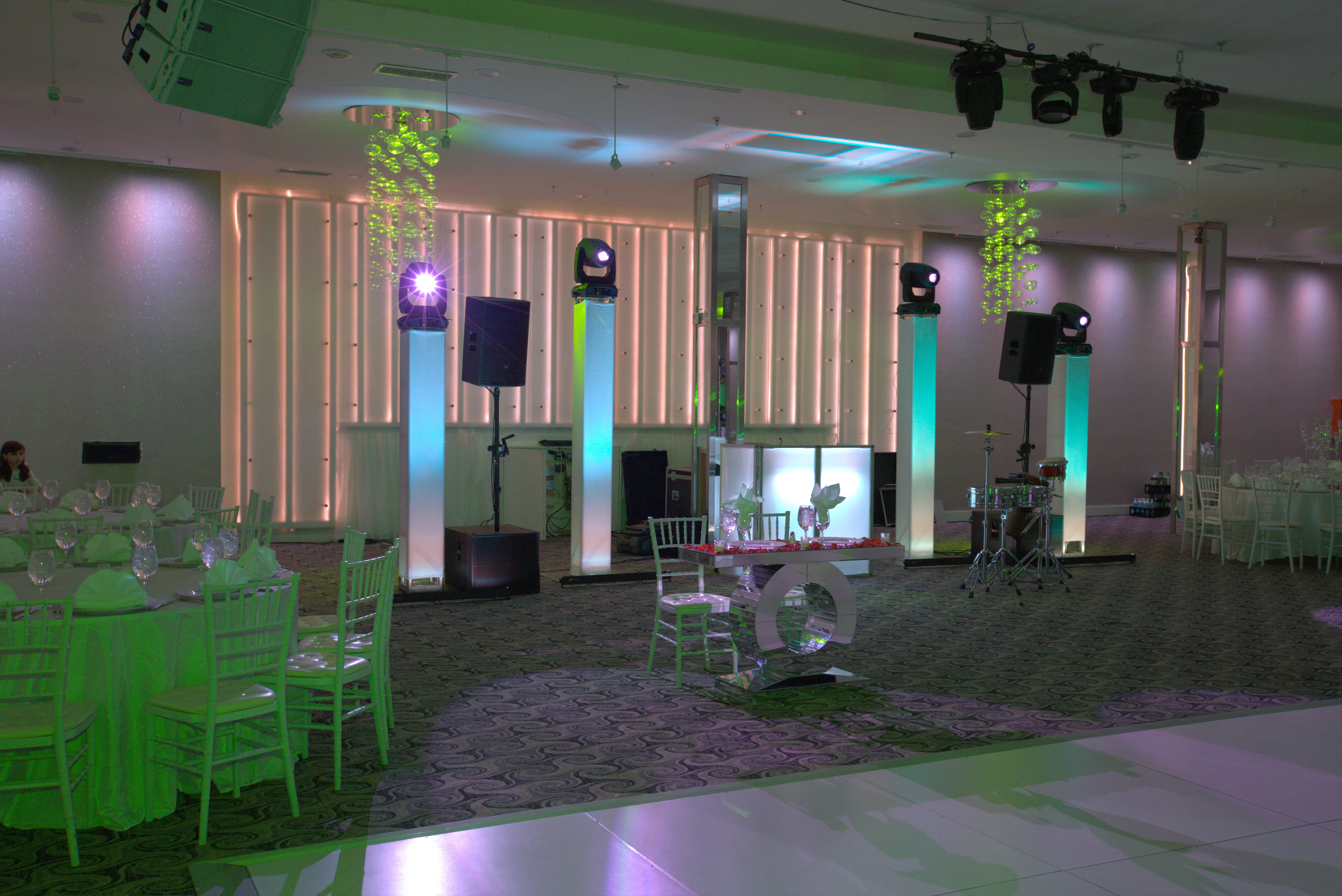 Ballroom with a lit DJ booth, two powered speakers on lit pedestals, a subwoofer and moving head lights