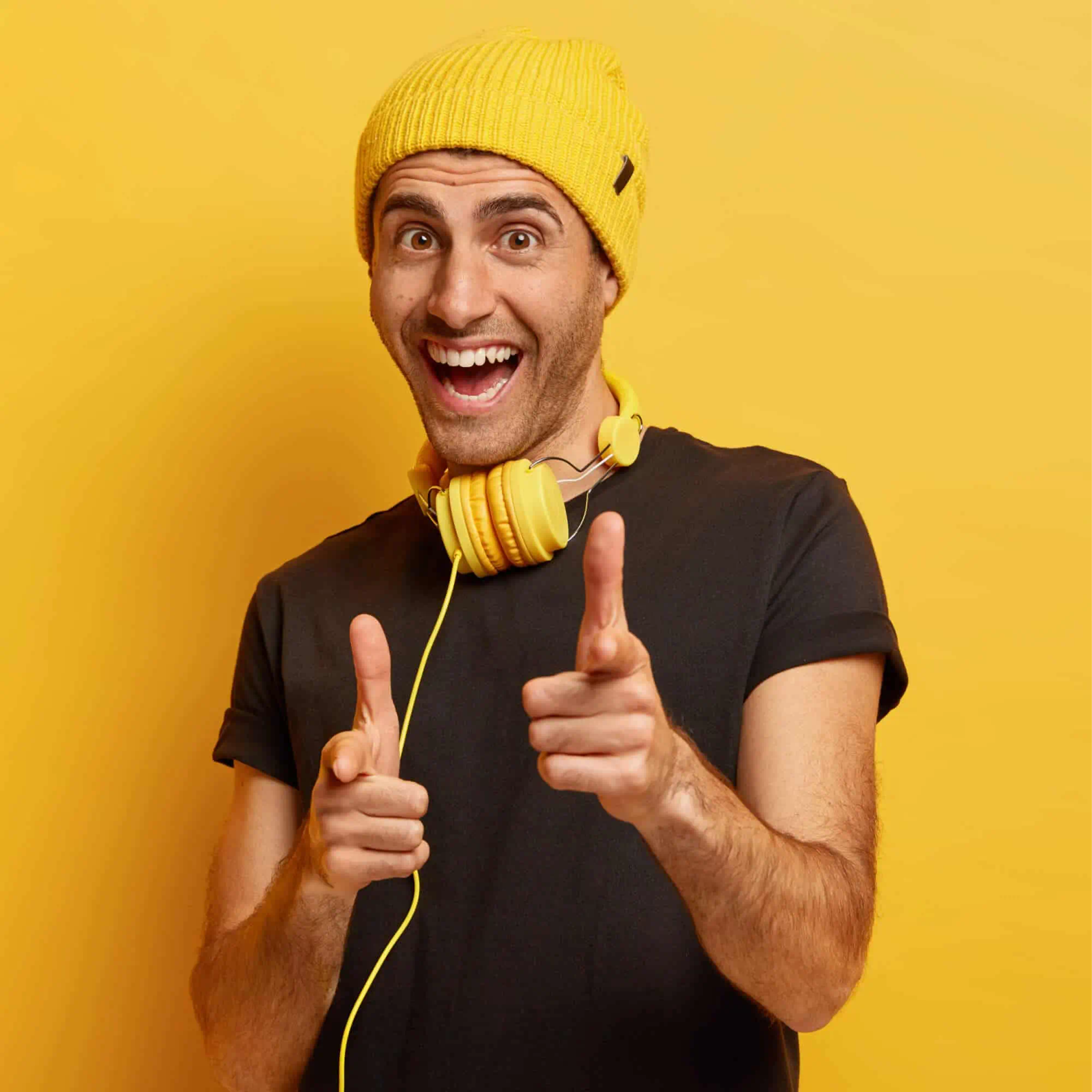a man wearing yellow hat and yellow headphones pointing at camera